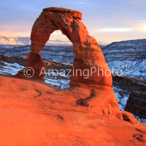 雪景色を背景に夕日に映えるデリケートアーチ